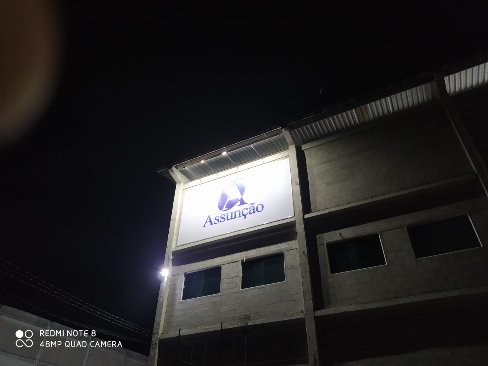 Letreiro luminoso Assunção instalado em fachada, vista noturna